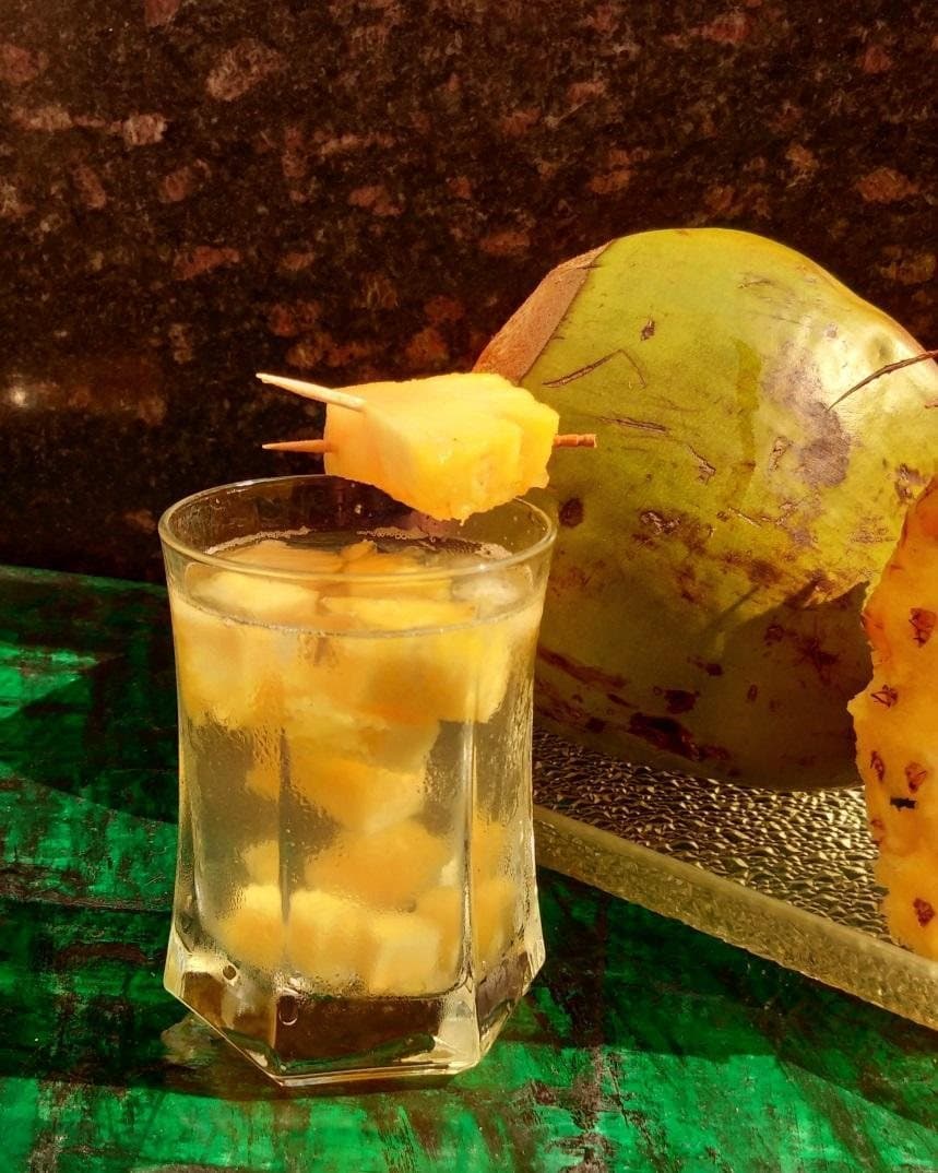 A glass of pineapple and coconut water garnished with a pineapple chunk, beside a tender coconut.